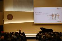 Rebecca Louise Smith bei ihrem Poetry Slam auf der Bühne der Neuen Aula. Neben ihr der Flügel, vor ihr das Publikum im Halbdunkel.