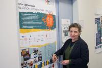 Die über den DAAD finanzierte Gastdozentin Dr. Sarah Creider steht vor einer Tür auf der ein Plakat mit Inhalten über die internationalen Kooperationen und Projekte der HSE hängt. Sarah Creider schaut und lächelt dabei in die Kamera.