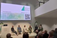 Auf einer Bühne sitzen sechs Personen, die an der Podiumsdiskussion zur Eröffnung der Karlsruhe School of Education teilnehmen. Auf einer Beamer-Projektionsfläche über ihren Köpfen werden sie namentlich vorgestellt als Ministerin Petra Olschowski, Prof. Dr. Nadine Anskeit (KSE), Prof. Dr. Thorsten Bohl (TüSE), Prof. Dr. Marita Friesen (HSE) - die außerdem gerade in ein Mikrofon spricht - , Prof. Dr. Thomas Riecke-Baulecke (ZSL) und Moderatorin Juliane Langer.