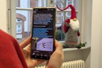 Eine Person schaut sich auf ihrem Smartphone den Auftakt-Post der Heidelberg School of Education bei der Social-Media-Plattform Linkedin an. Im Hintergrund sieht man auf einer Fensterbank einen Weihnachtswichtel mit langem Bart und großer Mütze stehen.