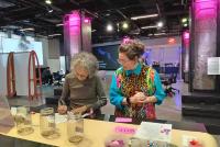 Prof. Nancy Lesko, PhD und eine ihrer Assistentinnen vom Teachers College der Columbia University, New York treffen letzte Vorbereitungen für einen Workshop im Smith Leaning Theater. Sie stehen an einer Lerntheke, auf der sich verschiedene Behältnisse und weitere Schreib-, Kleb- und Bastelutensilien befinden.