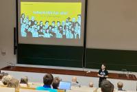 Prof. Dr. Christian Spannagel beginnt in einem voll besetzten Hörsaal seine Keynote für den Heidelberger Informatiklehrkräftetag. Im Hintergrund sieht man auf einer Projektionsfläche den Titel seines Vortrag "Informatik für alle!".