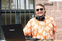 Dr. Thomas Renkert aka "DJ Tanzminister" mit Sonnenbrille am Mischpult; die Kopfhörer um den Hals