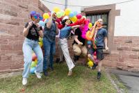 Das mit Federboas, Sonnenbrillen und anderen lustigen Requisiten versehene MINT-ProNeD-Team springt an der Fotobox in die Höhe; im Hintergrund der Ballonbogen zum HSE-Jubiläum.