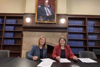 KerryAnn O'Meara, Provost und Dean des Teachers College, und Prof. Dr. Frauke Melchior, Rektorin der Universität Heidelberg, unterzeichnen an einem Schreibtisch im Teachers College das Memorandum of Understanding. Im Hintergrund Regale mit blauen Büchern, darüber ein Porträt.