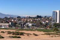 Blick auf die Stadt mit Hochäusern. Im Vordergrund Strand und grün bewachsene Dünen, hinten die Berge.