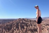 Eine junge Frau un Wanderkleidung blickt von einem Aussichtspunkt auf die vor ihr liegende Atacama-Wüste.