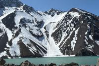 Das Bild zeigt einen schneebedeckten Berg im cajon del maipo, davor ein Bergsee, unter blauem Himmel.