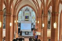 Blick von oben auf Referentin Theresa Heyd und ihre Startfolie "Queerfeindlichkeit im Klassenzimmer" in der Peterskirche.