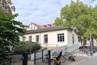 Das HSE-Gebäude in der Voßstraße 2 unter blauem Himmel mit Blick auf die Rampe und den Fahrradständer, gerahmt vom begrünten Campus Bergheim..